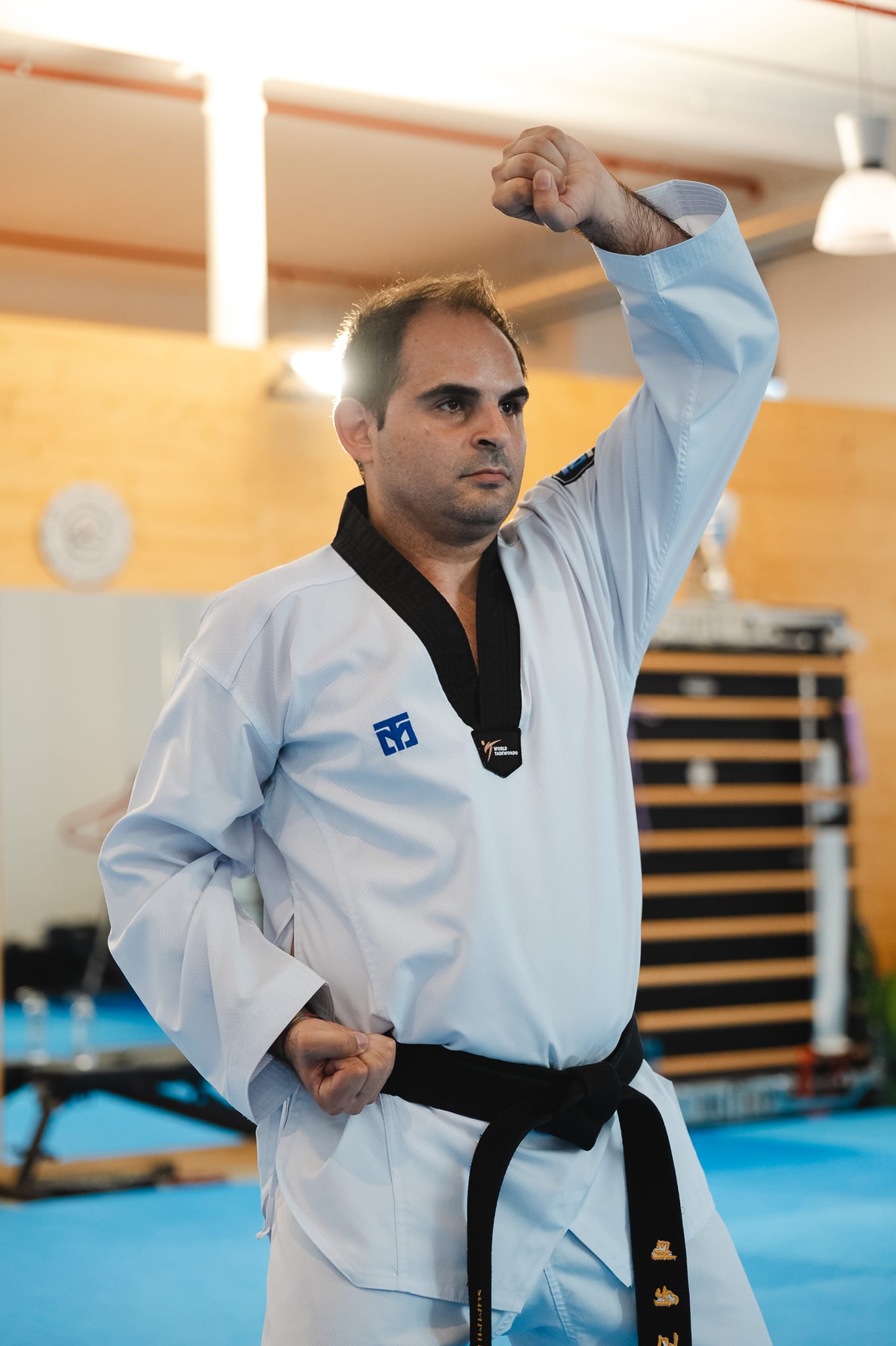 Cintura nera in dobok bianco esegue una tecnica di forma con il pugno alzato sopra la testa, sguardo concentrato