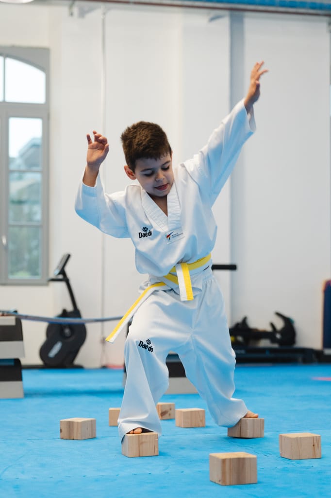 Bambino con cintura bianco-gialla si allena in equilibrio su blocchi di legno colorati