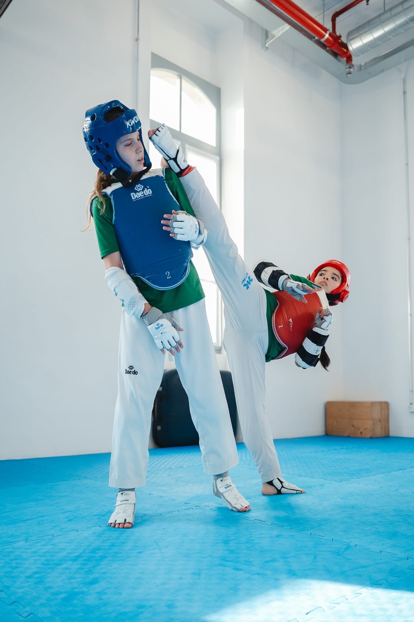 Calcio alto dell'atleta con casco rosso che raggiunge il casco dell'avversaria in blu durante un incontro di combattimento